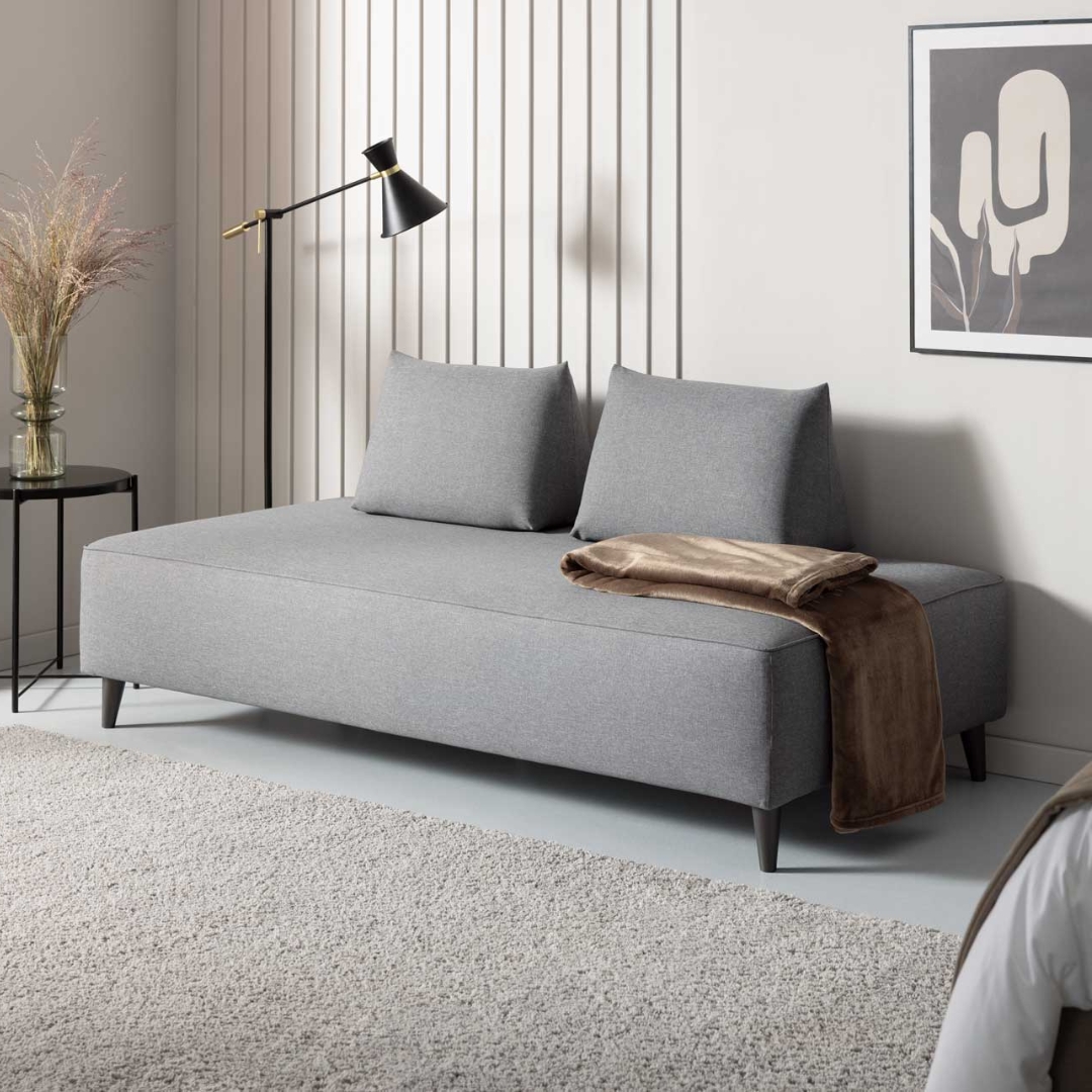 Schlafcouch Bardolino mit grauem Bezugstoff und zwei Sirmione Kissen im Hotelzimmer
