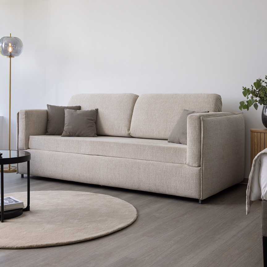 Das Etagensofa Meran mit hellem, creme-farbenen Bezugsstoff steht im Showroom und sieht wie ein normales Zweisitzer-Sofa aus, da es nicht aufgeklappt ist.