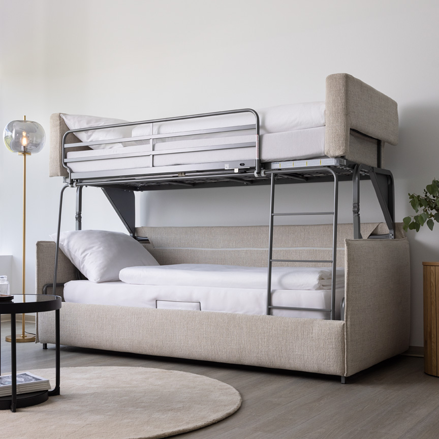 Das Etagensofa Meran mit hellem, creme-farbenen Bezugsstoff steht aufgeklappt im Showroom.