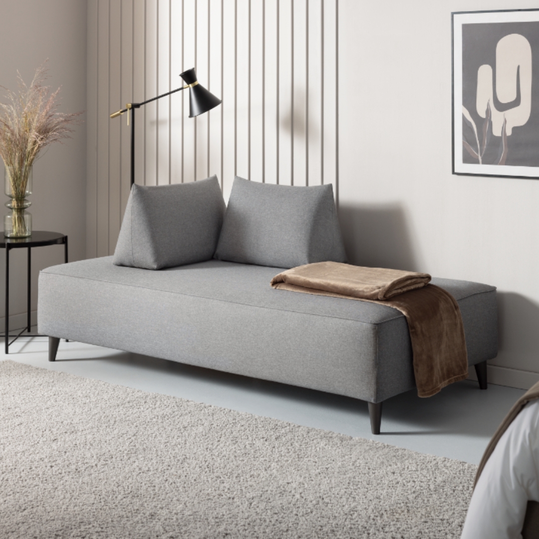 Schlafcouch Bardolino mit grauem Bezugstoff und zwei Sirmione Kissen im Hotelzimmer